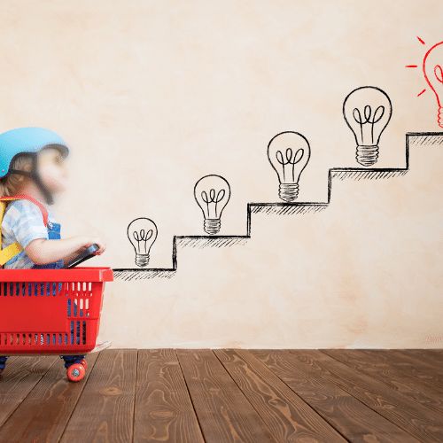 Little girl sitting a basket with wheels and rocket strapped to the back. In front of her are steps with lightbulbs on - the last bulb is red being her goal